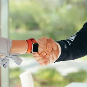 Close-up of a handshake between two adults, one wearing a smartwatch, set in an outdoor environment.